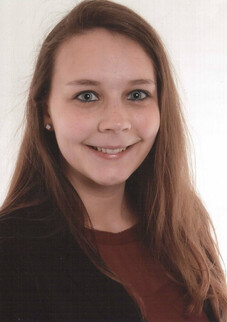 Katharina Klug mit langen braunen Haaren und Lächeln vor hellem Hintergrund.